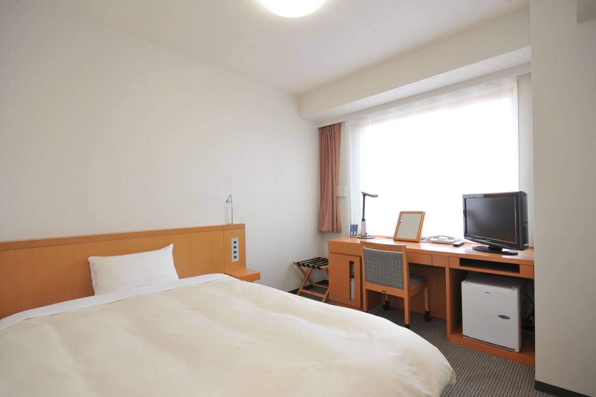 A hotel room with a bed, a desk, a television, and a small refrigerator.