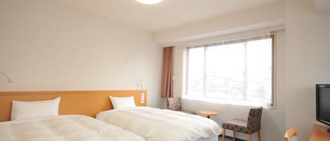 A hotel room with two beds, a TV, a small table, and a window with curtains.