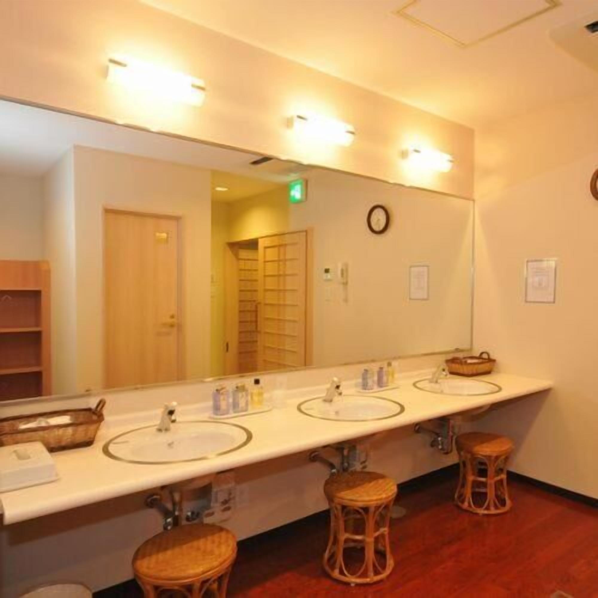 A hotel bathroom with three sinks, a large mirror, and wicker stools.