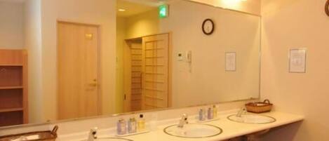 A hotel bathroom with three sinks, a large mirror, and wicker stools.