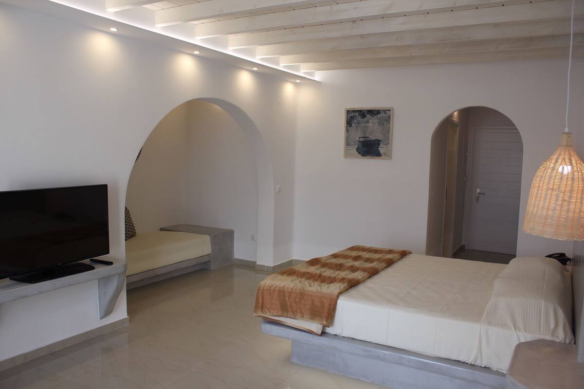 Ein modernes Schlafzimmer mit Bett, Fernseher und Sitzgelegenheit.