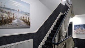 A staircase with black and white checkered carpet, white walls, and a painting of a beach scene. - Hotel 33 (Blackpool)