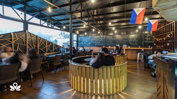 A restaurant interior with high ceilings, exposed beams, and wooden accents. Tables and chairs are arranged for dining. - 3BU Hostel Baguio (Baguio)