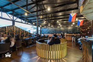 A restaurant interior with high ceilings, exposed beams, and wooden accents. Tables and chairs are arranged for dining. - 3BU Hostel Baguio (Baguio)