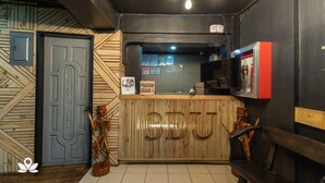 A reception desk with a wooden finish and the letters "BBU" prominently displayed. There are two wooden sculptures on either side of the desk, and a bench is visible to the right. - 3BU Hostel Baguio (Baguio)