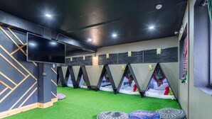 A room with a green artificial turf floor, a flat-screen TV mounted on the wall, and a row of sleeping areas with headboards. - 3BU Hostel Baguio (Baguio)