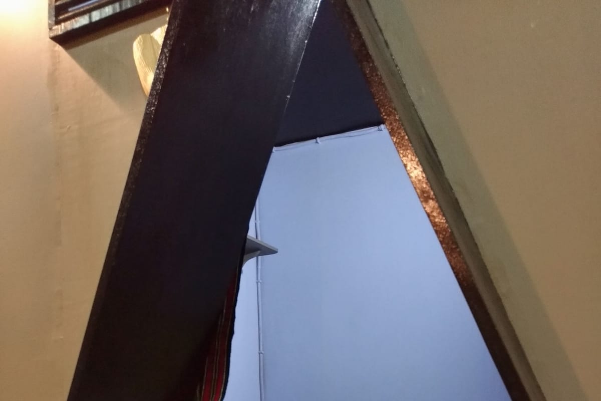 Un espacio pequeño y triangular para dormir con una cama, una colchoneta verde y un aplique de pared.
