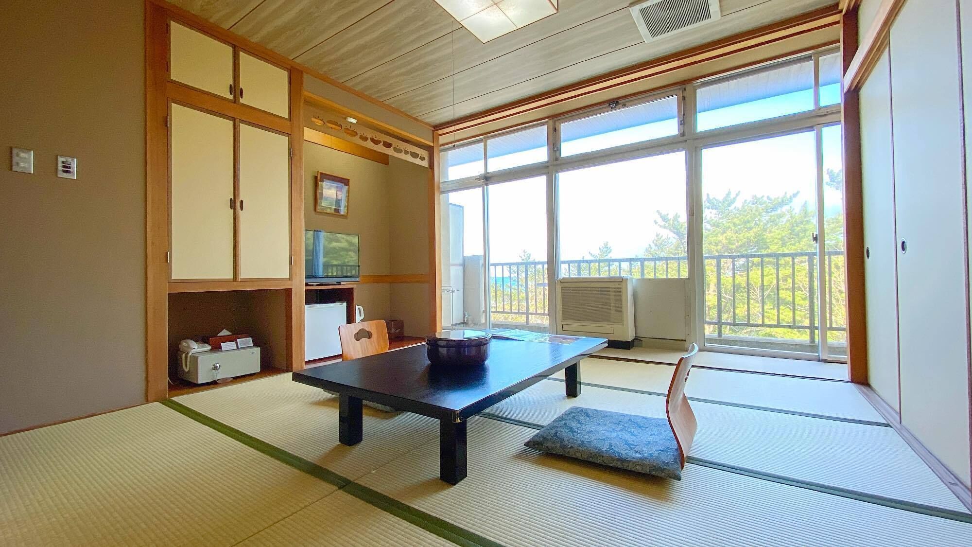 A tatami mat room with a low table, a cushion, a TV, and a sliding door to a balcony.