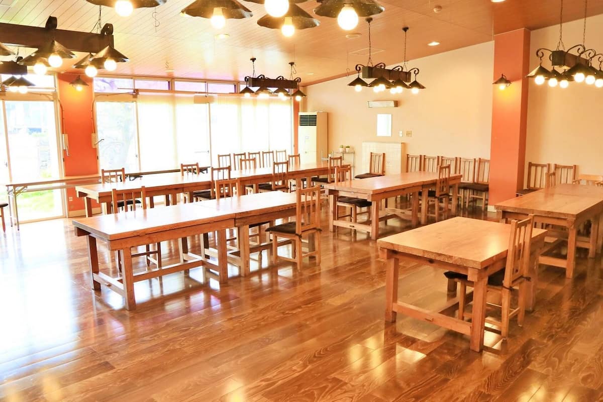 Un amplio comedor con varias mesas y sillas de madera, ventanas grandes y lámparas colgantes.