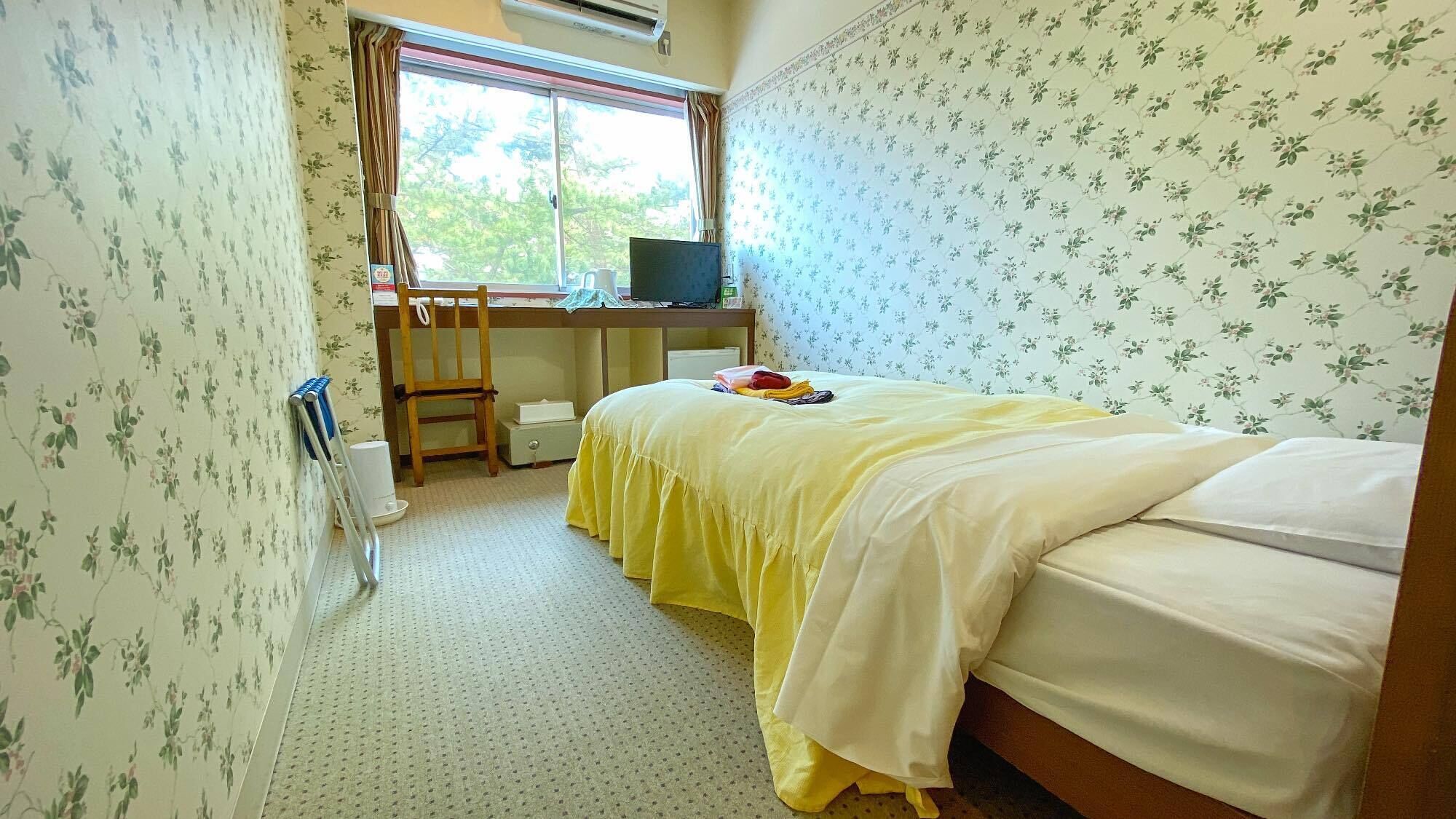 A bedroom with a bed, a desk with a computer, a chair, and a window.