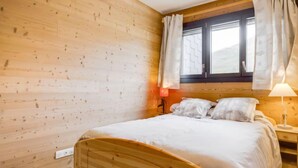 A wooden room with a bed, a window with curtains, and a nightstand with a lamp. - Champ Bozon by Interhome (La Toussuire)