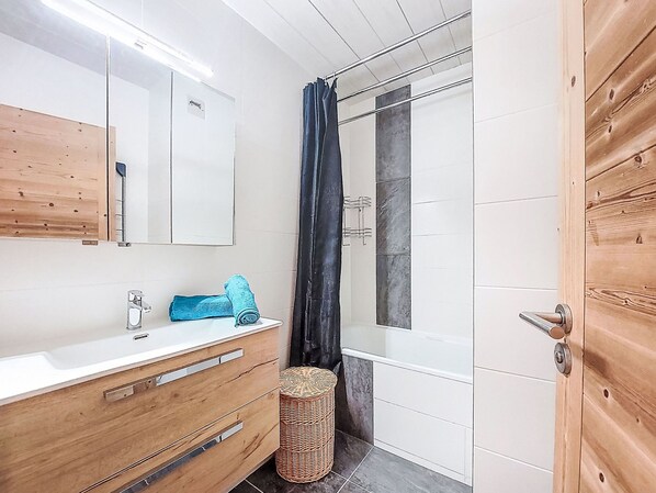 A modern bathroom with a wooden vanity, a shower with a curtain, and a wicker stool.