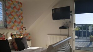Un dormitorio con cama, un radiador, un televisor montado en la pared y una ventana con persianas.