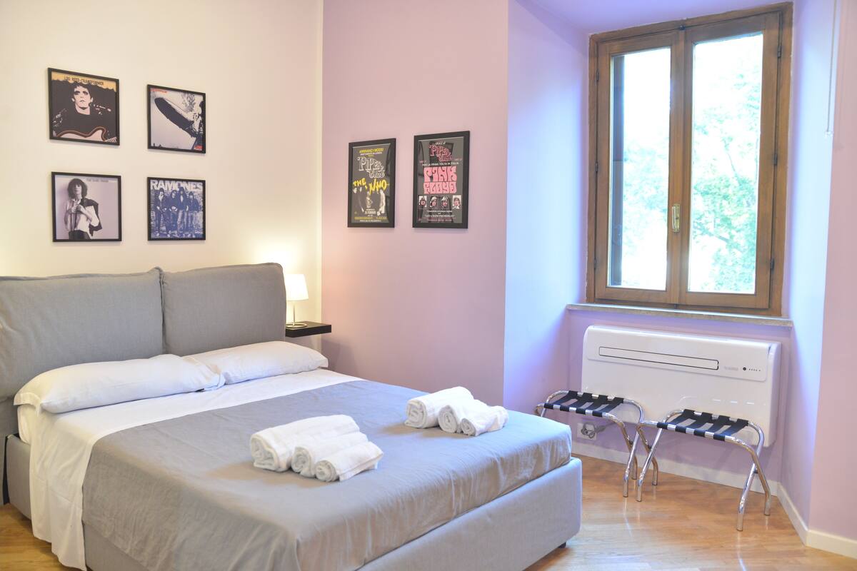 A bedroom with a bed, a radiator, a window, and four framed posters on the wall.