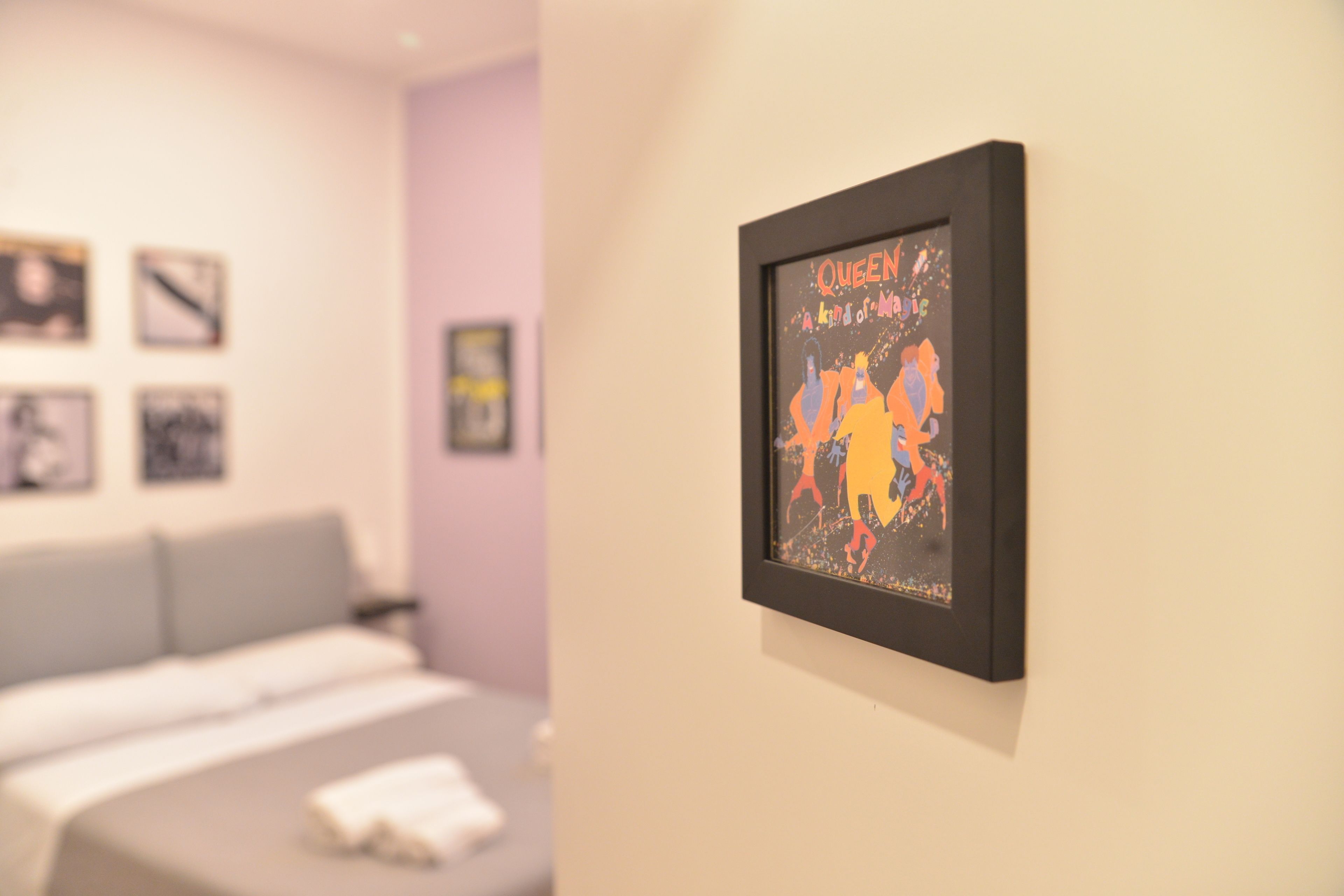 A hotel room with a bed, a framed artwork on the wall, and a wall-mounted light fixture.