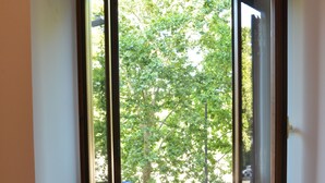 A room with a small table and two chairs, a window with a view of trees, and a white wall. - All You Need Is Rome Guesthouse (Rome)
