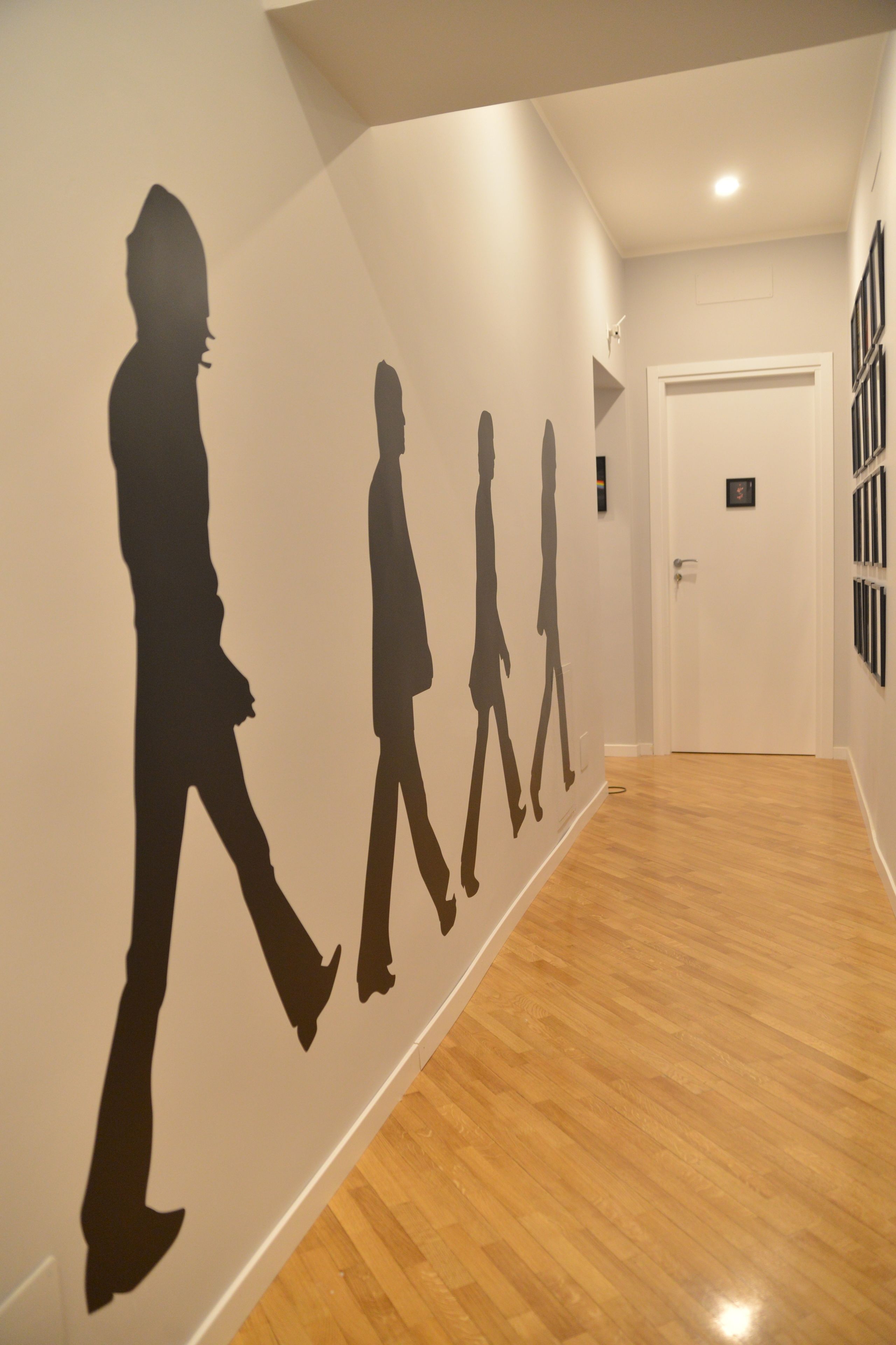Un pasillo con suelo de madera y un muro con siluetas de personas caminando.