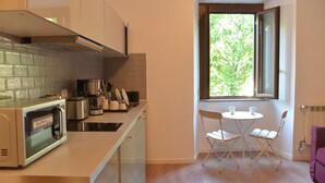 A compact kitchen with a microwave, toaster, and coffee maker. There is a window with a view of trees and a purple chair in the corner. - All You Need Is Rome Guesthouse (Rome)