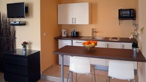 A compact kitchen with white cabinets, a built-in oven, a sink, and a small dining area with two chairs. - Galini beach studios (Corfu)