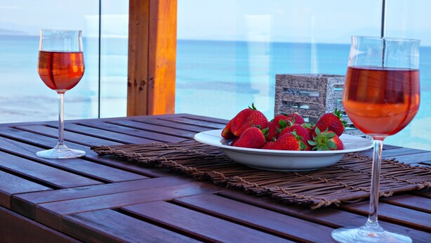 A wooden table with two wine glasses and a bowl of strawberries. - Galini beach studios (Corfu)