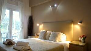 A neatly made bed with pillows, a bedside table with a lamp, and a view of the outdoors through a window. - Galini beach studios (Corfu)
