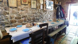 Une salle à manger aux murs de pierre, avec une longue table dressée pour un repas, où l’on trouve une variété de plats et d’accompagnements.