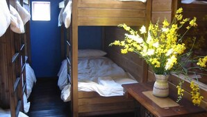 Een slaapkamer met stapelbed, een raam, een houten tafel met een vaas gele bloemen, en een naaimachine.