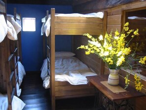 Une chambre avec un lit superposé et une fenêtre, une table en bois ornée d’un vase de fleurs jaunes, et une machine à coudre.