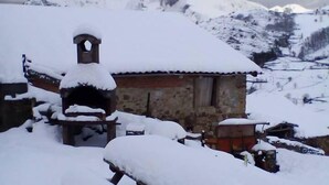 Un bâtiment rustique, avec un toit enneigé et un clocher, entouré de montagnes recouvertes de neige.