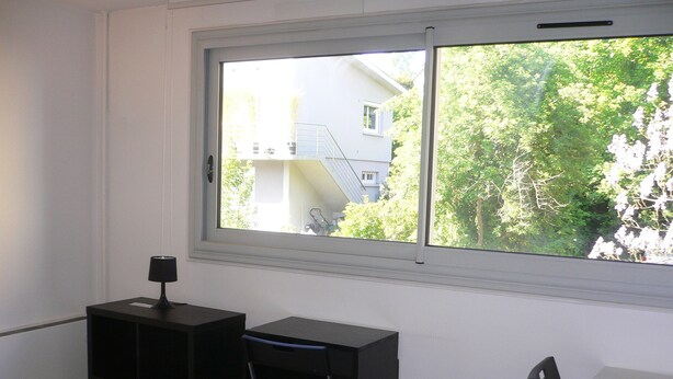 Une pièce comprenant un bureau, une chaise et une fenêtre donnant sur un quartier résidentiel.