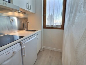 Una cocina compacta con lavavajillas Bosch, un fregadero y una ventana con vistas a árboles.