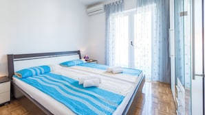 A neatly made bed with blue and white bedding, a bedside lamp, and a window with curtains. - Honolulu Apartment (Dubrovnik)