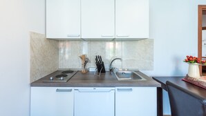 A compact kitchen with white cabinets, a stainless steel sink, and a marble backsplash. - Honolulu Apartment (Dubrovnik)