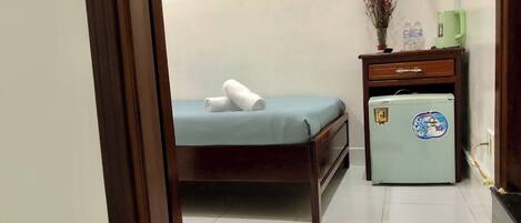 A small room with a bed, a refrigerator, a red mat, and a door.