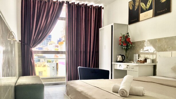 Une chambre d’hôtel avec un lit, un bureau, une chaise, un petit canapé et une fenêtre avec des rideaux.