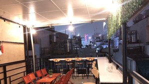 Un espace de restauration aménagé sur le toit, avec plusieurs tables et chaises, un canapé et une vue sur le paysage urbain la nuit.
