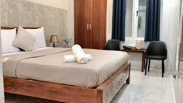 Ein Hotelzimmer mit einem Holzbett, einem Schreibtisch mit Stuhl, einem Fenster mit Vorhängen und einem Kleiderschrank.