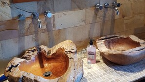 A bathroom with a wooden basin sink, a large mirror, and a stone wall. - Casona Los Gamonales (Carreno)
