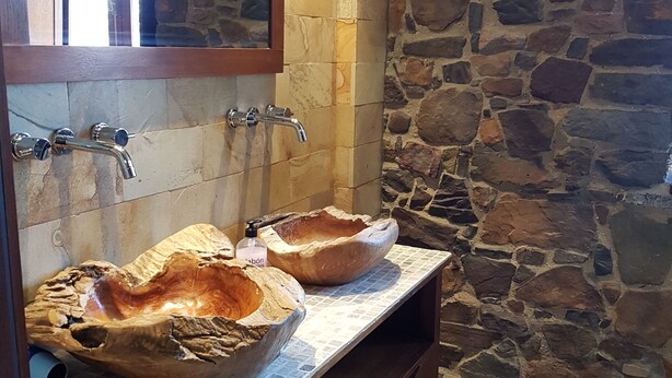 A bathroom with stone walls, two wooden bowls as sinks, a mirror, and a wooden cabinet. - Casona Los Gamonales (Carreno)