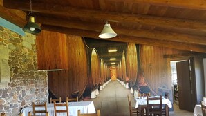 A long corridor with wooden barrels lining the walls, tables and chairs set up for dining, and hanging lights. - Casona Los Gamonales (Carreno)