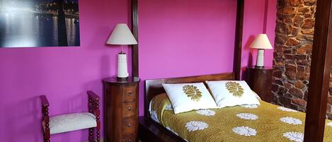 Quarto com cama de dossel, mesa de cabeceira com abajur, cadeira e quadro na parede.