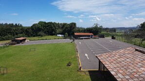 A parking lot with a clear sky, green grass, and a building with a red roof. - Casona Los Gamonales (Carreno)