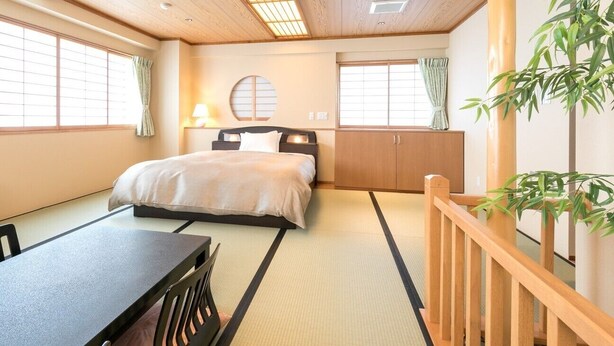 A traditional Japanese-style room with tatami flooring, a bed with a wooden headboard, a table, and a desk. - Hotel C&i Koriyama (Koriyama)