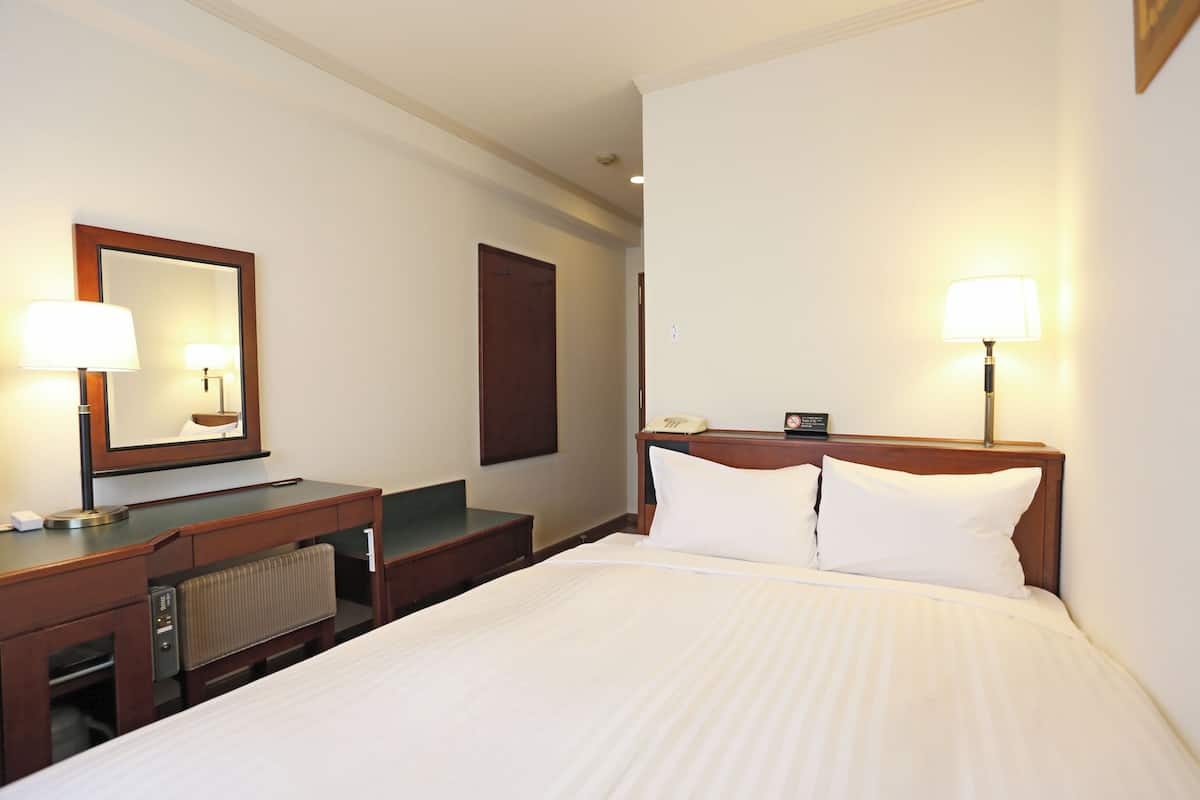 Een hotelkamer met een bed, een bureau met telefoon, een spiegel en twee bedlampjes.