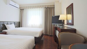 Ein Hotelzimmer mit zwei Betten, einem Schreibtisch mit Lampe, einem Fernseher und einem Spiegel.