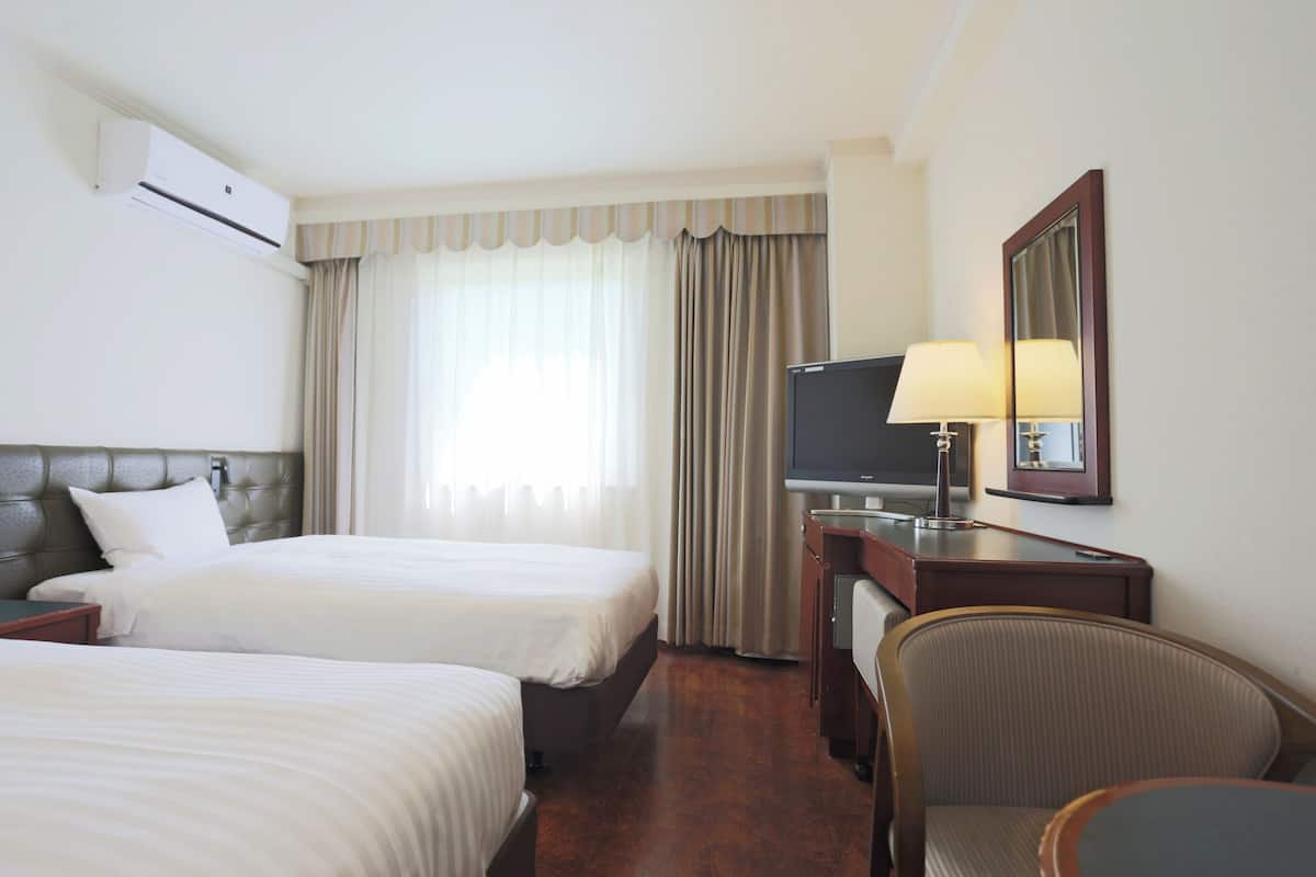 Een hotelkamer met twee bedden, een bureau met lamp, een televisie en een spiegel.