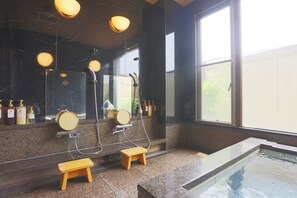 Ein modernes Badezimmer mit einem großen Spiegel, zwei hölzernen Hockstühlen, einer Duschkabine und einem kleinen Pool.
