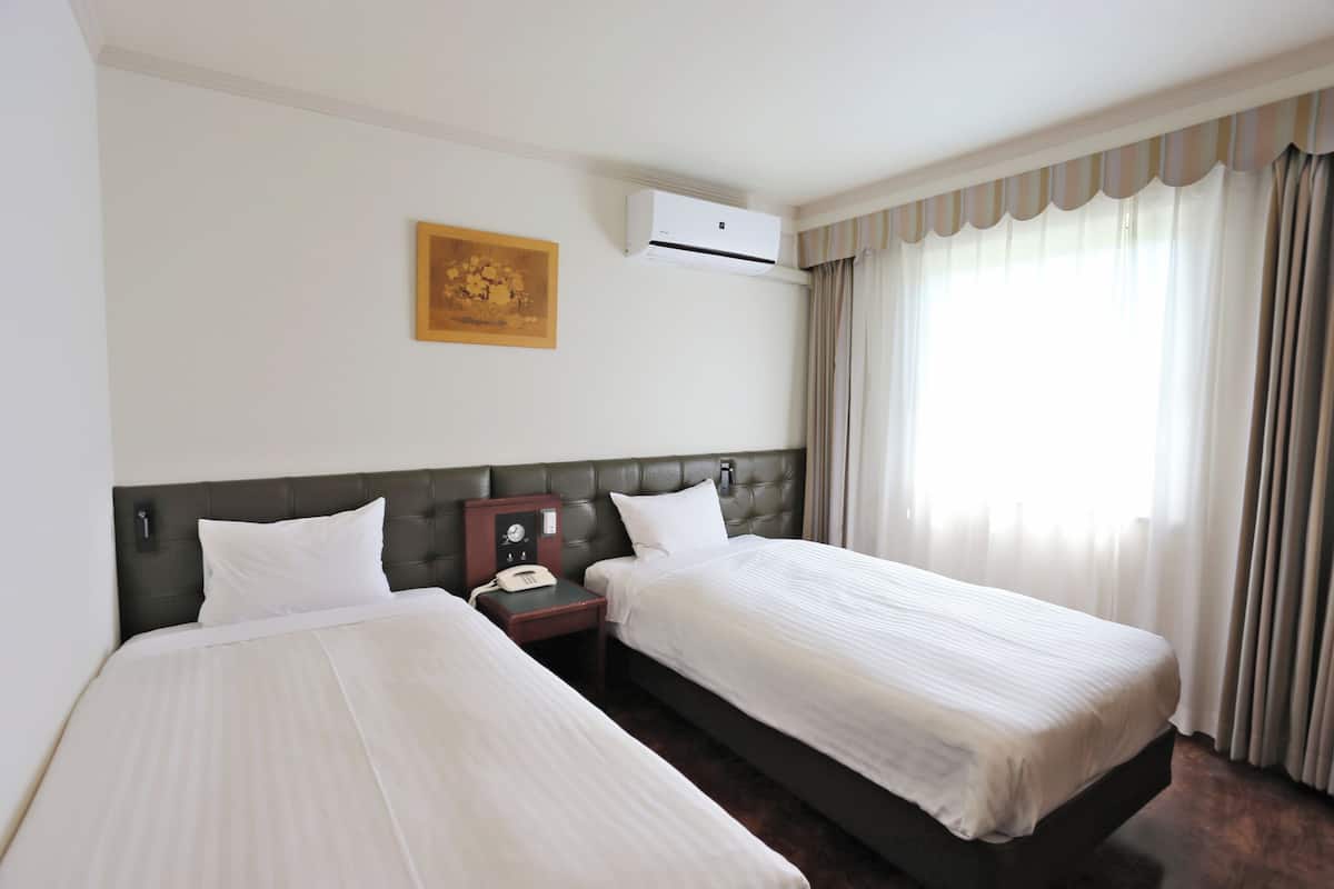 Een hotelkamer met twee bedden, een luchtverkoeler aan de muur, een klok en een schilderij.