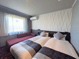 Habitación de hotel con una cama grande, un sofá, una ventana con cortinas y un aire acondicionado de pared.
