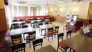 Ein Restaurant mit mehreren Tischen und Stühlen, einer roten gepolsterten Bank und einer Theke mit einer Speisekarte.
